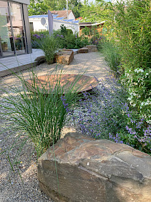Garten in Paderborn aus wassergebundener Wegedecke mit Wasserschale aus Cortenstahl, Grauwackefindlingen, Holzterrasse und Bepflanzung aus Gräsern, Stauden und Bambus.