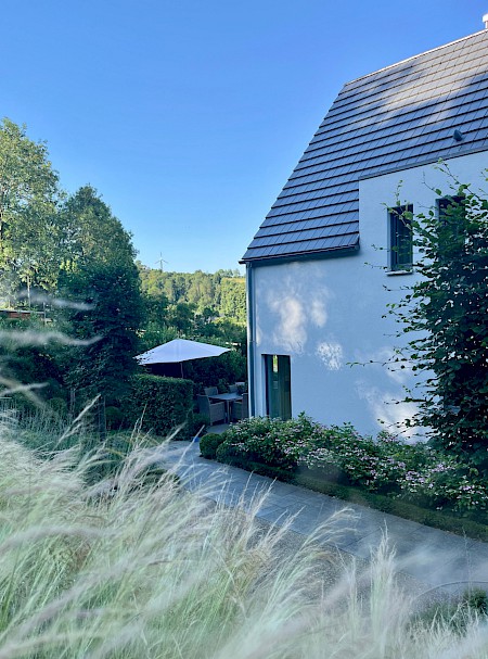 Modernes Haus in Borchen mit klassisch gestaltetem Privatgarten in Hanglage, mit flächiger Bepflanzung aus Gräsern und Hortensien.