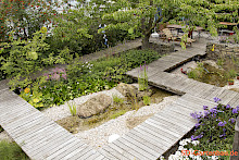 Gartengestaltung in Borchen mit Holzstegen, einem Bachlauf mit Natursteinfindlingen und dichter Staudenpflanzung.
