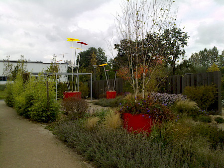 Schaugarten auf der Landesgartenschau in Rietberg mit roten Pflanztöpfen, bunter Staudenbepflanzung und Holzzaun aus Eichenbalken im Hintergrund.