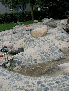 Modelierte Hügel aus Natursteinpflaster mit Granitfindlingen als Wasserspielbereich eines Kindergartens in Paderborn.