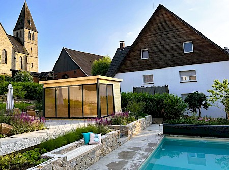 Pool in einem Privatgarten in Lichtenau mit Trockenmauern aus Muschelkalk und einem Gartenhaus.