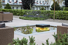 Eckiger Teich mit einem beleuchteten Quellstein auf einer Gastronomieterrasse in Bad Lippspringe.