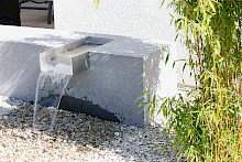 Detail eines modernen Wasserspiels in Paderborn mit einem maßgefertigten Granitblock und intergerierter Wasserschütte aus Edelstahl.