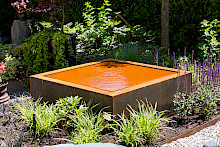 Beet mit einem quadratischem Wasserspiel aus Cortenstahl in einem Privatgarten in Paderborn.
