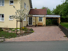 Einfahrt aus rotem Betonpflaster mit angrezendem Beet und Krustenplatten aus Sandstein.