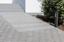 Eingang eines Hauses in Boorchen mit Blockstufen und Stelen aus Granit, daneben eine Pflasterung aus gerompelten Betonpflaster.