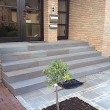 Eingang eines Hauses in Paderborn aus Grauwackblockstufen sowie angrenzender Pflasterung aus Grauwackeplatten und einer Einfahrt aus Klinkerpflaster.