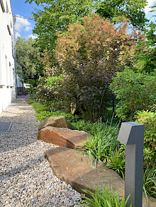 Kiesweg um ein Haus in Paderborn aus Lippekies mit Grauwackefindlingen und angrenzender Bepflanzung.