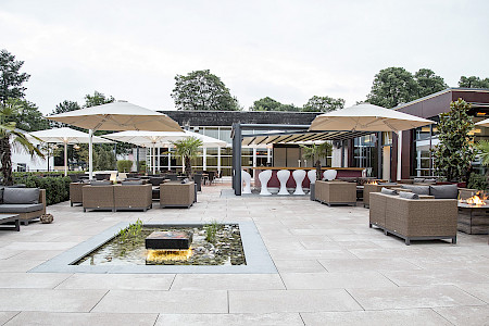 Gastronomieterrasse in Bad Lippspringe aus großformatigen Betonplatten und einem Wasserbecken gerahmt von Natrusteinplatten in Granit. Im Wasserbecken befindet sich ein quadratisch gesägter Quellstein.