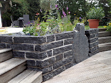 Hochbeet aus Palisaden in Basalt und einem integrierten Findling aus Schiefer.