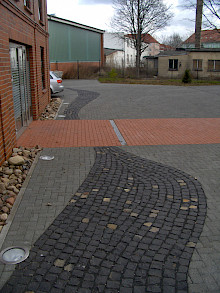 Eingangsbereich aus Klinkerpflaster und Parkplätze sowie Zufahrt in Betonpflaster gepflastert. Dazwischen ein geschwungenes Band aus Basaltkleinpflaster.