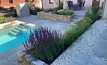 Poolgarten mit großformatigen Betonplatten, Trockenmauern aus Muschelkalk und Lippekies ziwchen den Schrittplatten.