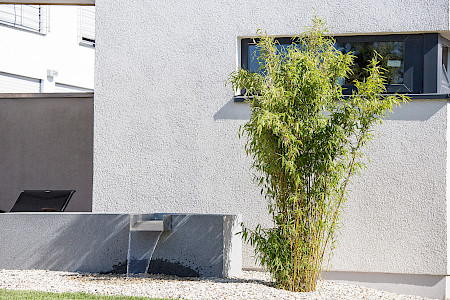 Moderner Garten in Paderborn mit einem rechteckigen Quellstein aus Granit und einem daneben stehenden Bambus.
