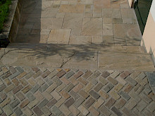 Terrasse aus Sandsteinplatten im römischen Verband sowie Weg aus Natursteinpflaster im Fischgrätmuster.
