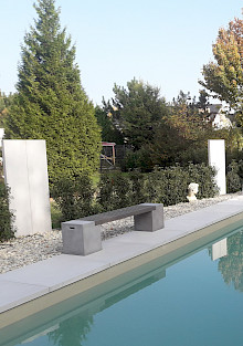Pool mit angrenzender Umrandung aus großformatigen Betonplatten sowie Stelen aus Sichtbeton als Sichtschutzelemente.