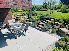 Terrasse in Lichtenau mit großformatigen Betonplatten in Sichtbeton und angrenzender Hanggestaltung mit Grauwackefindlingen.