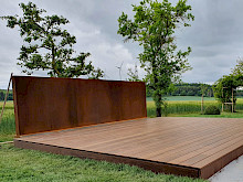 großzügige Holzterrasse mit Sichtschutzwänden aus Cortenstahl.