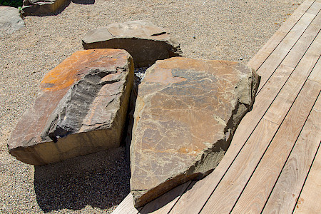 Detail einer Holzterrasse in Paderbron mit eingelassenen Findlingen und angrezender wassergebundener Wegedecke.