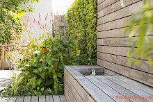 Kleiner Garten in Paderborn mit einer maßgefertigten Sitzbank inklusive Sichtschutz aus Holz. In der Sitzbank ist ein individuell gefertiges Wasserspiel aus Edelstahl integriert.