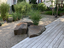 Holzterrase mit integrierten Natursteinfindlingen und Bepflanzung aus Gräsern in einem Garten in Paderborn.