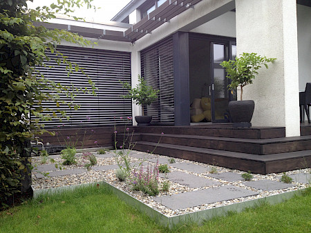 Terrasse mit angrenzender Treppe aus geöltem Holz und angrenzendem Kiesbeet in einem Privatgarten in Paderborn.