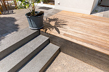 Detail eines Senkgartens in Paderborn mit einer Treppe aus Natursteinblockstufen, einer Stahlwange aus Cortenstahl und einem Holzdeck.