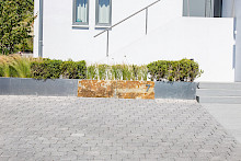 Vorgarten eines Einfamilienhauses in Borchen mit einem Hochbeet aus Aluminiumund integriertem Sandsteinfelsen. Bepflanzt ist das Hochbeet mit Gräsern und Buchsbaum.