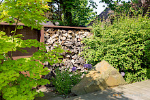 Holzlagerregale aus Cortenstahl mit umliegender Bepflanzung und einem Natursteinfindling im Vordergrund in einem Garten in Paderborn.