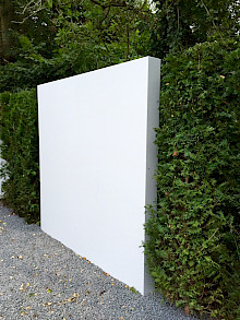 Helle Sichtschutzwand aus Metall in einer Bepflanzung aus Eiben.