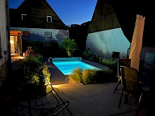 Garten mit beleuchtetem Swimmingpool, Gartenhaus und mehreren Pollerleuchten zur Wegebeleuchtung.