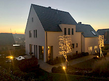Modernes Haus in Borchen mit Formgehölzen, die von Bodenstrahlern beleuchtet werden.