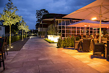 Gastronomieterrasse eines Hotels in Badlippspringe mit beleuchteten Pflanztöpfen, angestrahlten Bäumen und Lampen unter den Sonnenschirmen.