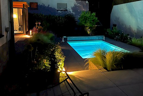 Garten mit beleuchtetem Pool, Gartenhaus und Terrasse in Paderborn.